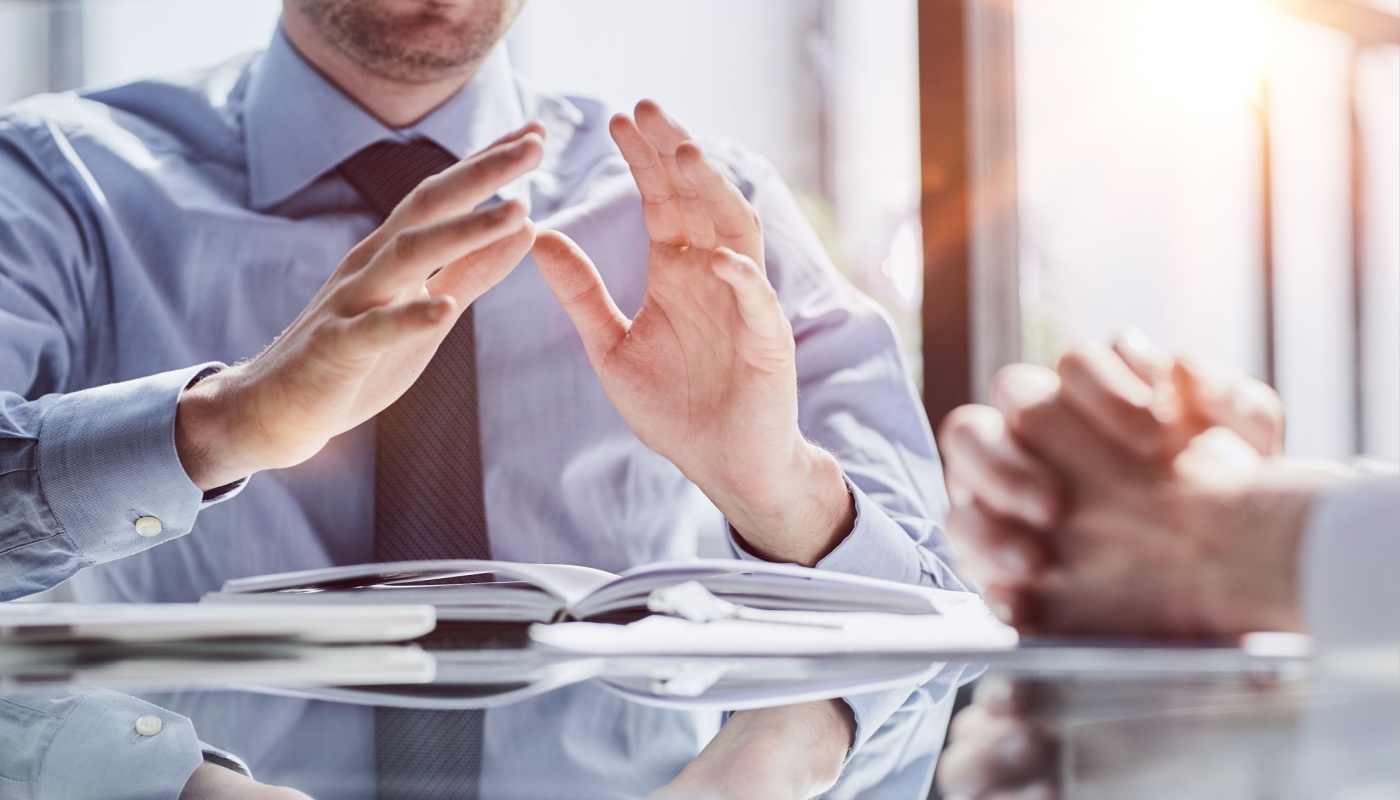 Two businessmen sit at desk discussing project details; clinical trial financial management concept